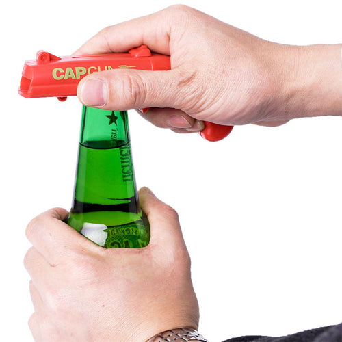 Person using a red cap gun to open a green bottle on a white background