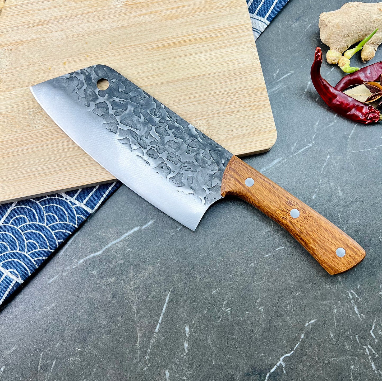 Chef's knife with wooden handle on a gray surface with a cutting board and ingredients.