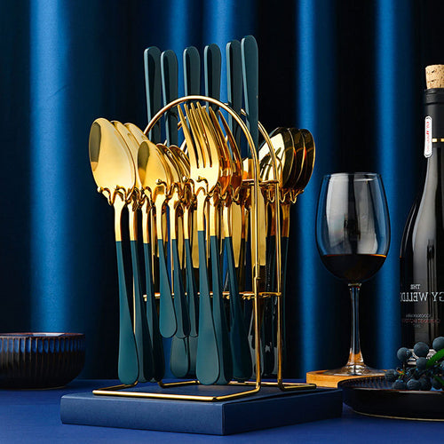 Set of gold and blue cutlery on a stand with a glass of red wine and a bottle in the background.