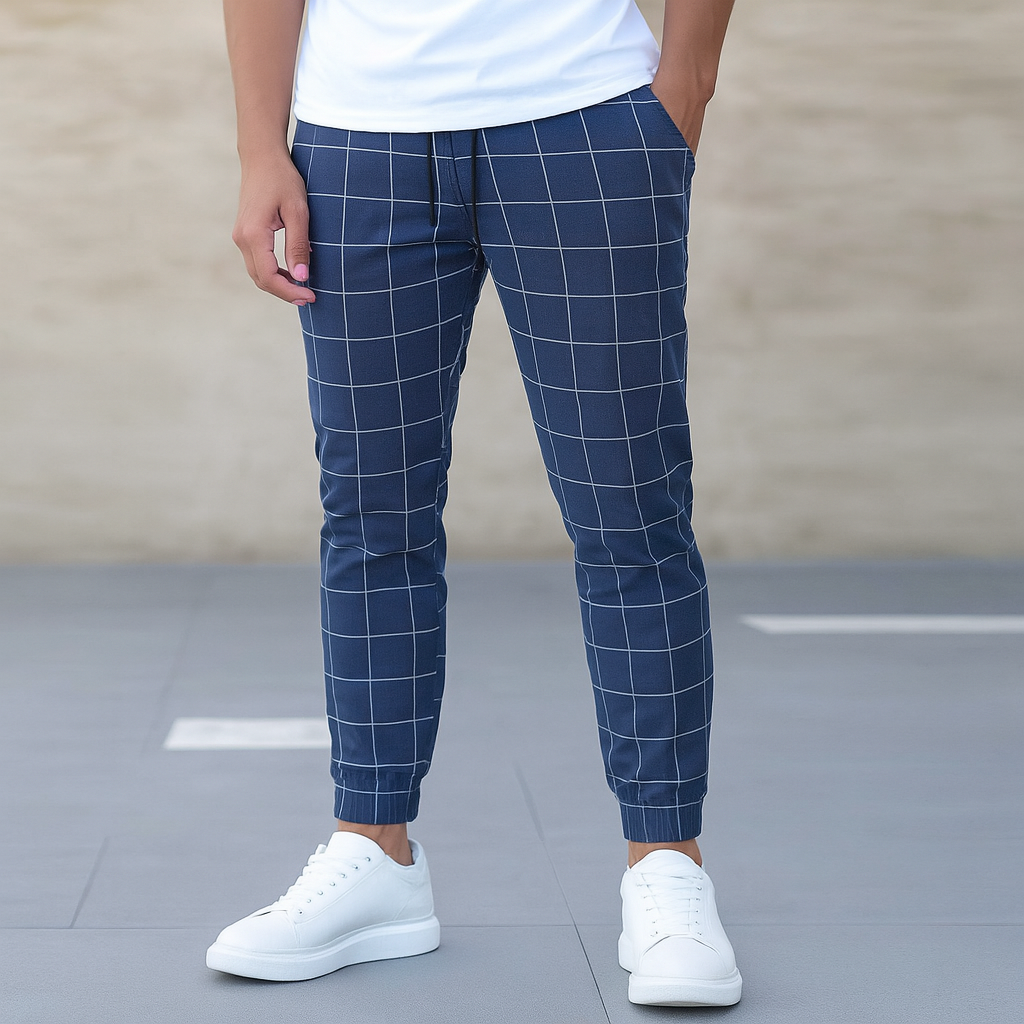 Person wearing blue checkered pants and white sneakers on a plain background