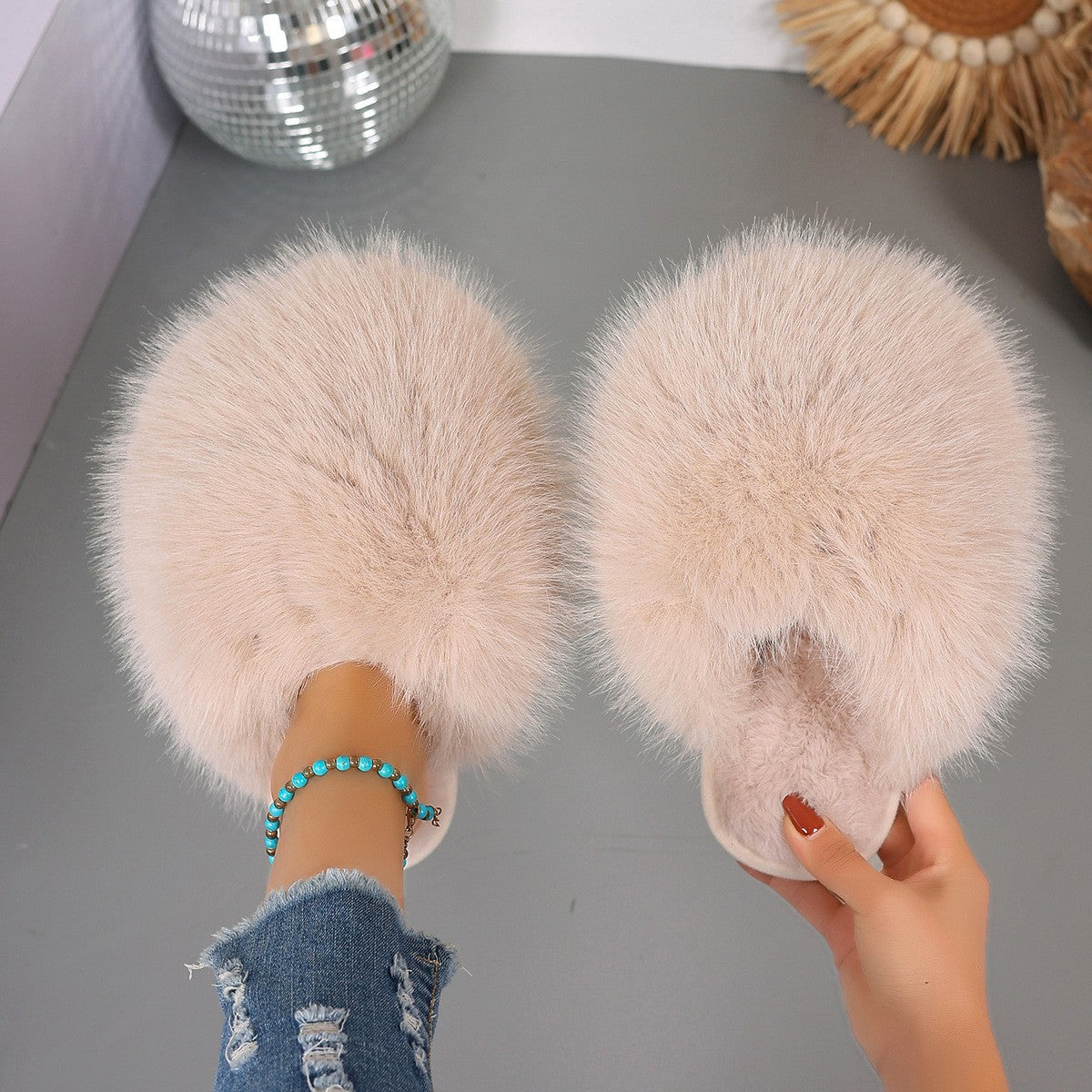 Person wearing fluffy slippers on a gray floor with decorative items in the background.