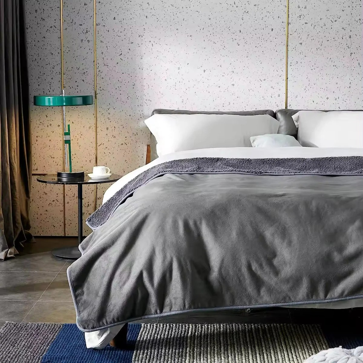 Bedroom with a bed covered in gray bedding, a side table with a lamp, and a textured wall.