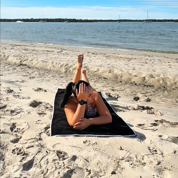Person lying on a towel at the beach with water and sky in the background