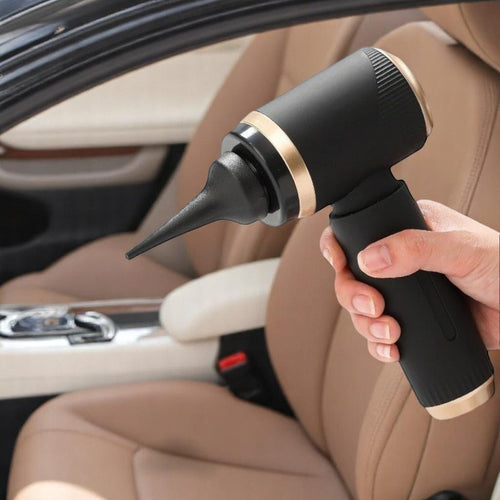 Hand holding a black and gold vacuum cleaner inside a car.