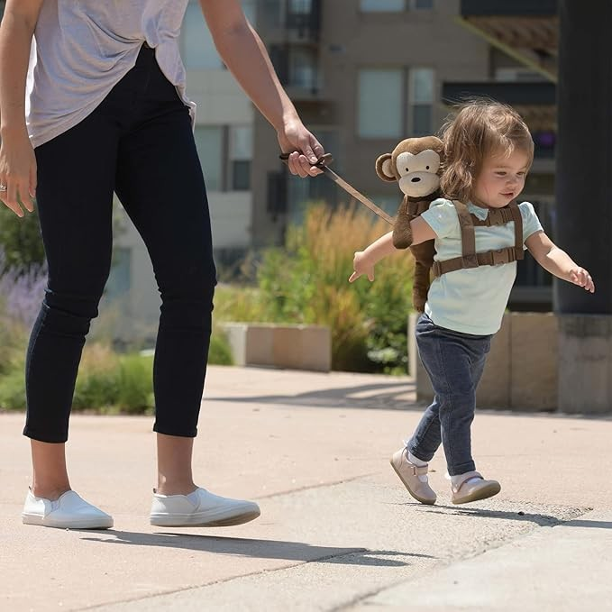 Child walking with a plush monkey toy on a leash held by an adult outdoors.