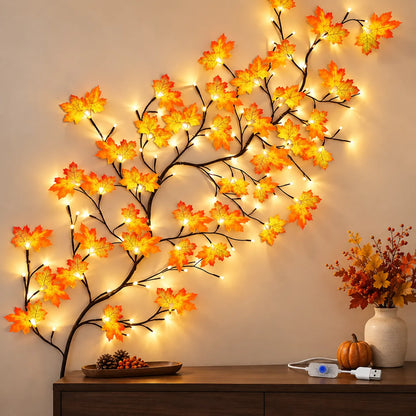 A decorative wall-mounted branch sculpture with glowing warm white string lights and orange-yellow autumn leaves, displayed above a wooden console table in a styled interior setting.