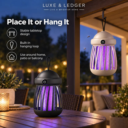 Two bug zapper lanterns by Luxe & Ledger shown in a home patio setting at dusk, one hanging from a porch beam and one placed on a wooden table. The product has a black top and base with a beige body, emitting a purple glow inside.