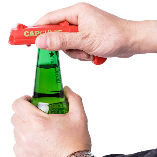 Person using a red cap gun to open a green bottle on a white background