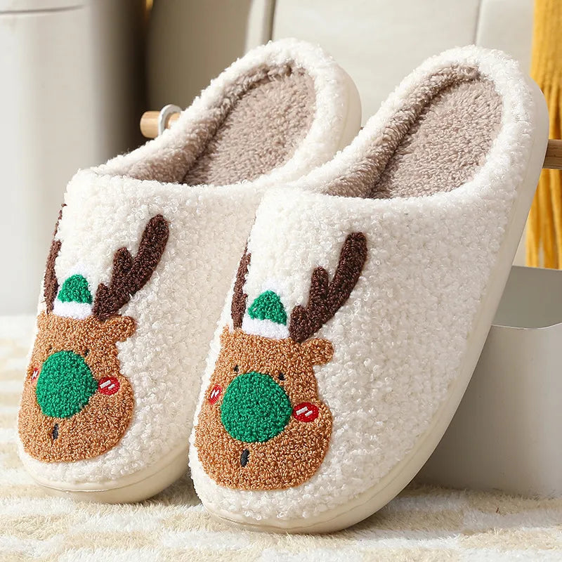 Pair of white slippers with reindeer face designs on a soft surface.