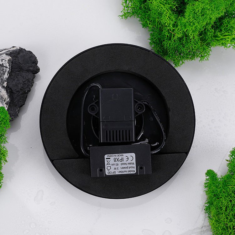 Black round electronic device on a white surface with greenery