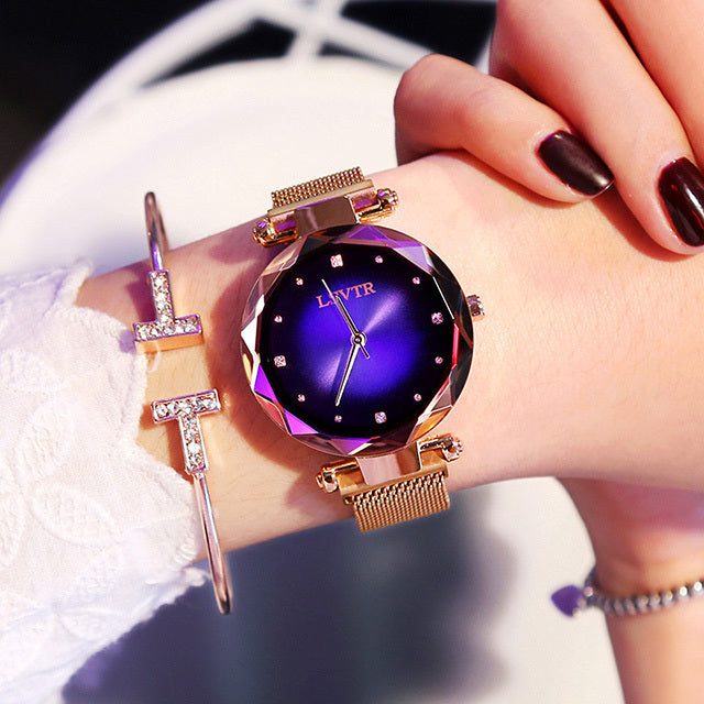 A woman's watch with a rose gold metal band and case, featuring a multicolored glass dial and a spiral crown.