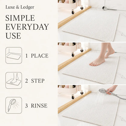 A white textured bath mat shown in a bathroom setting with text reading 'Lux & Ledger SIMPLE EVERYDAY USE' and three step icons for easy use: 1 place, 2 step, 3 rinse. A person's bare foot and hand are visible demonstrating the mat.