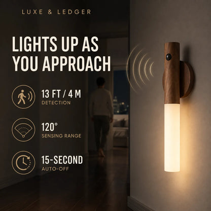 A Luxe & Ledger smart wall light shown mounted on a wall in a hallway at night, with a person walking away in the background. The light has a dark wood top and a glowing warm white cylindrical shade.