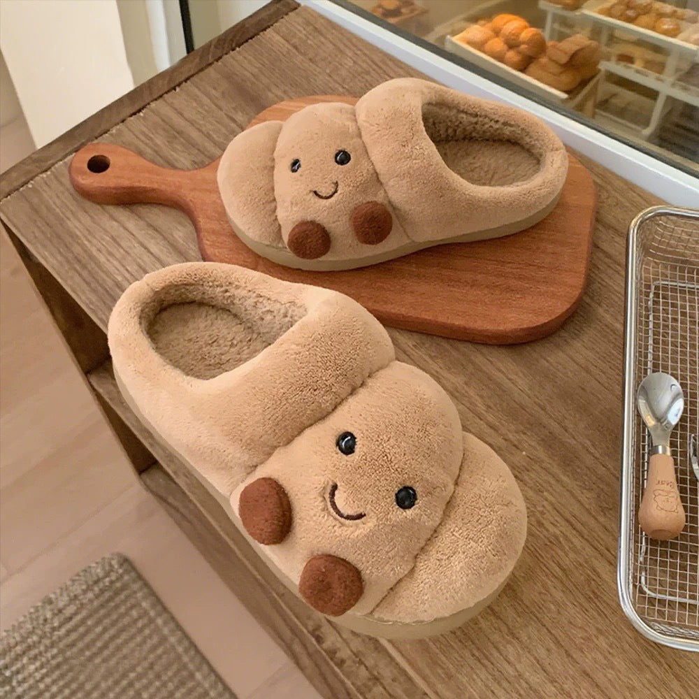 Pair of cute animal-shaped slippers on a wooden surface with a kitchen background.