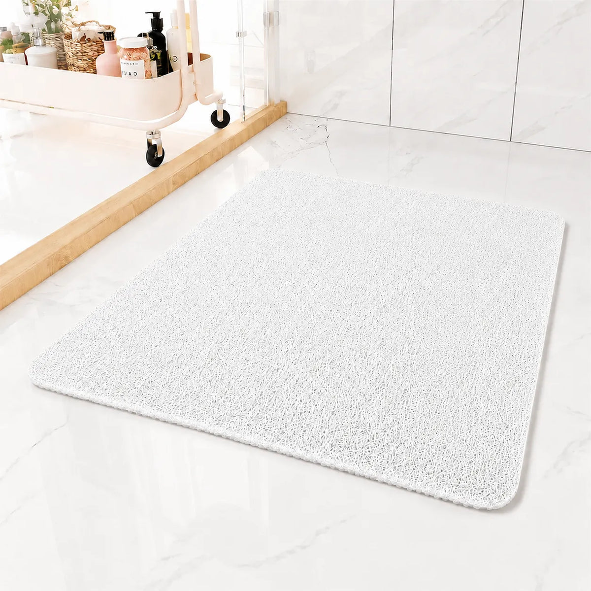 A rectangular white bath mat with rounded corners, shown on a glossy white marble bathroom floor next to a wooden baseboard and a small vanity cart.