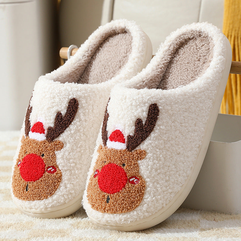 Pair of white slippers with reindeer face designs on a soft surface.