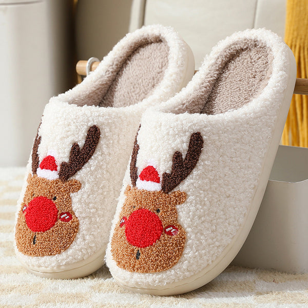 Pair of white slippers with reindeer face designs on a soft surface.