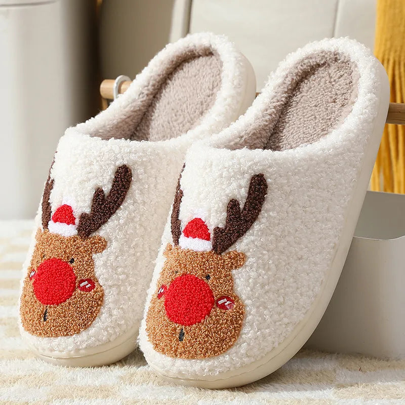 Pair of white slippers with reindeer face designs on a soft surface.