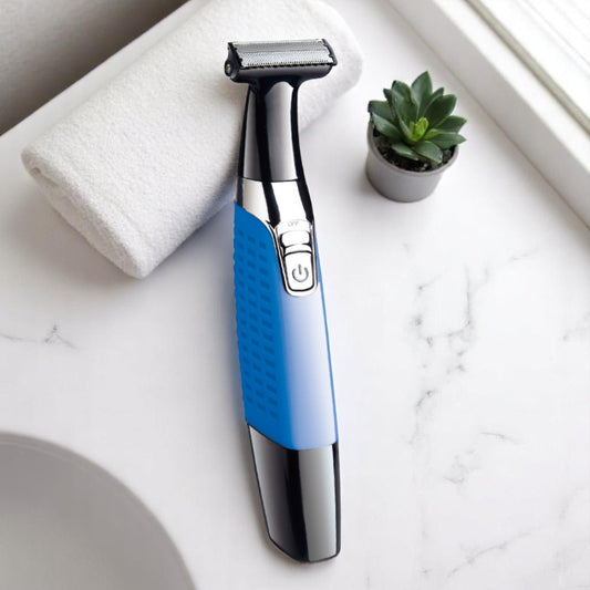 A blue and silver electric razor with a stainless steel blade, an ergonomic handle, and a USB recharge port, placed on a white surface next to a green plant and a white towel.