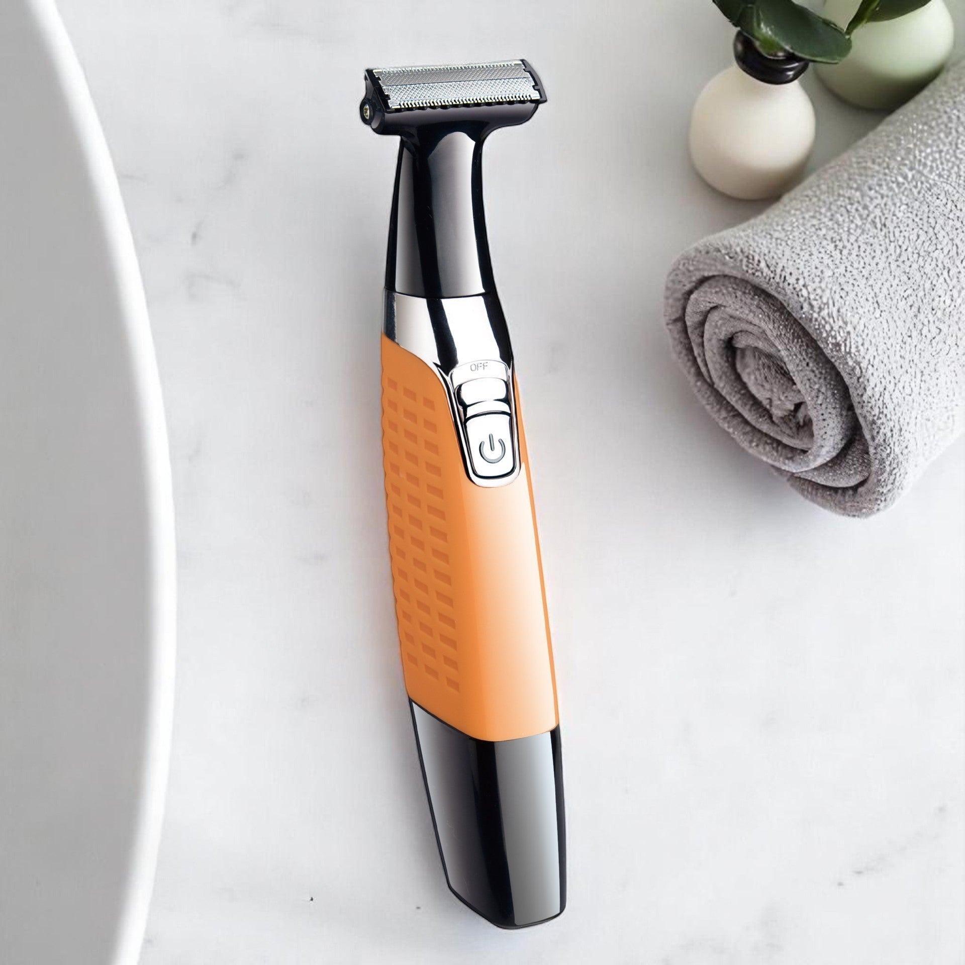 A blue and silver electric razor with a stainless steel blade, an ergonomic handle, and a USB recharge port, placed on a white surface next to a green plant and a white towel.