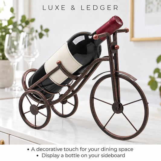 A wine bottle displayed on a decorative metal tricycle stand shaped like a bicycle, set on a white countertop in a bright kitchen or dining space. The stand is dark bronze with copper-toned accents.