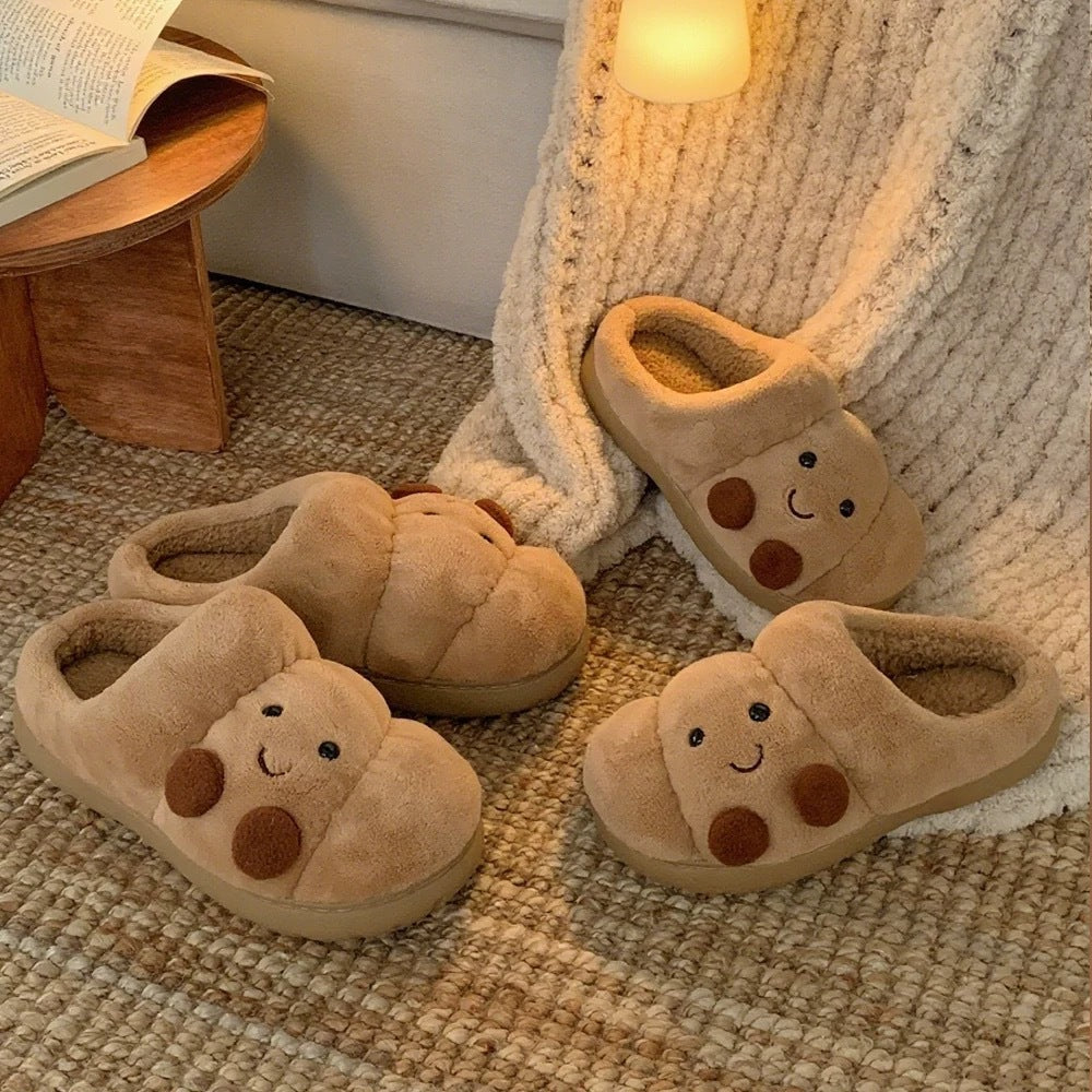 Pair of plush slippers with smiley faces on a textured surface next to a wooden stool and book.