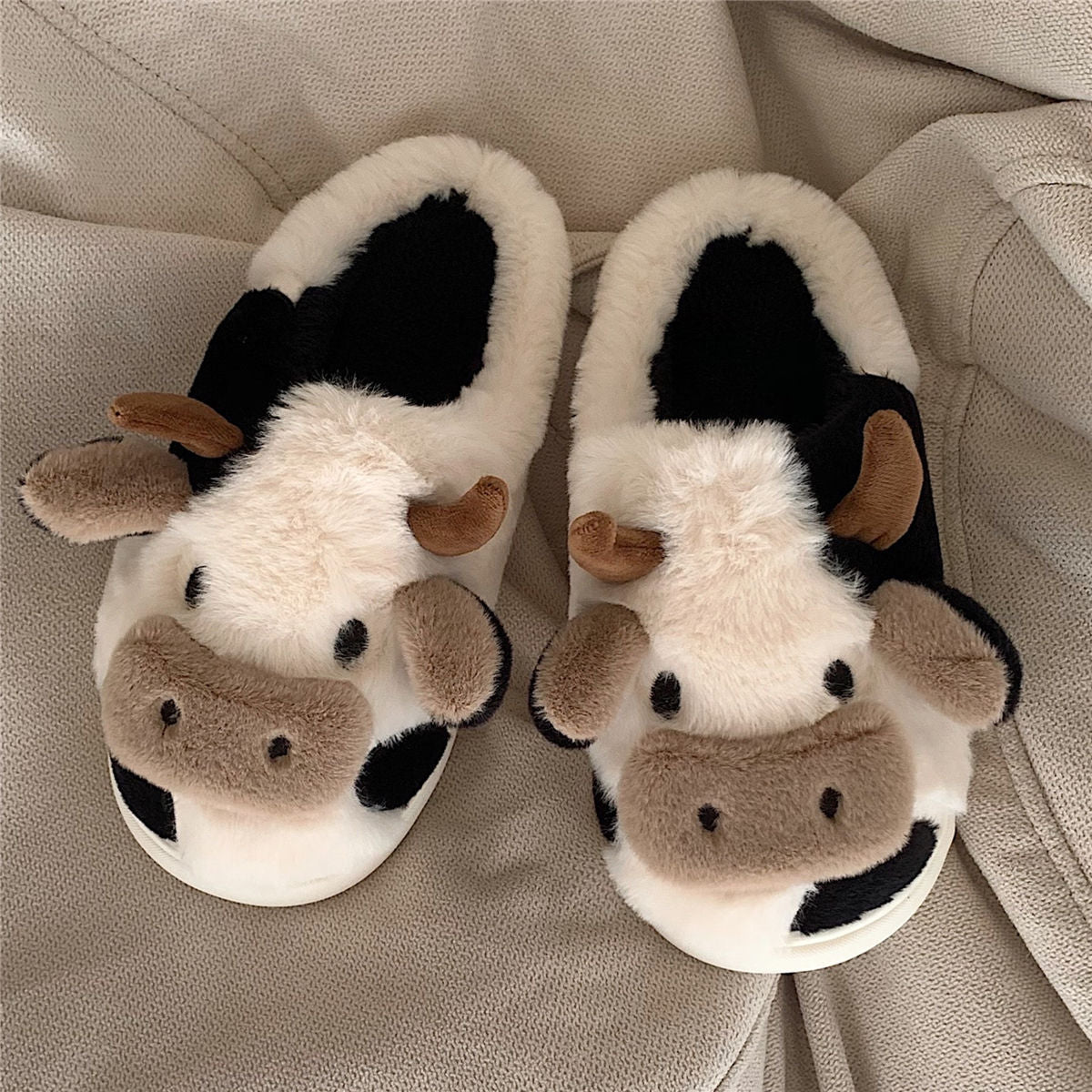 Pair of cow-themed slippers on a beige surface