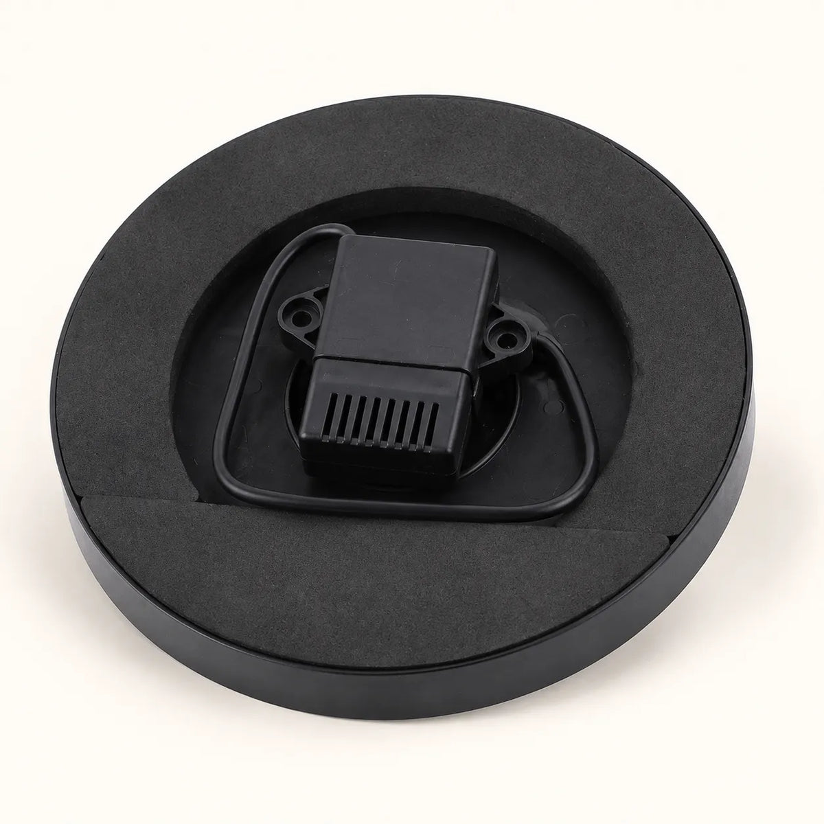 A black circular foam insert tray holding a small black plastic component with a ribbed vented section and looped tabs, photographed on a clean white background.