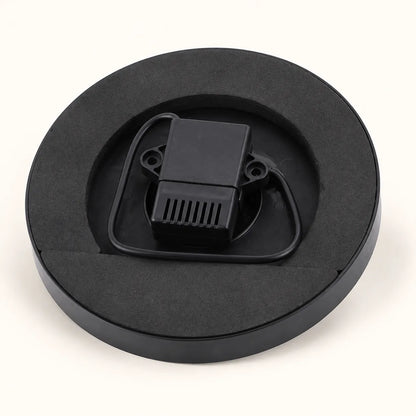 A black circular foam insert tray holding a small black plastic component with a ribbed vented section and looped tabs, photographed on a clean white background.