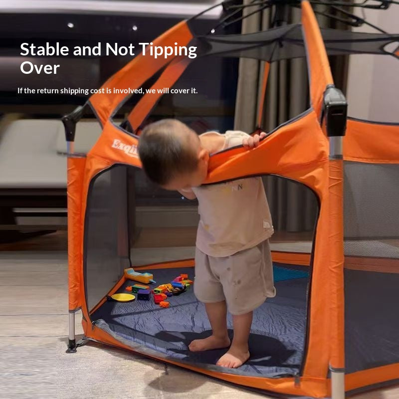 Child playing inside an orange and gray playpen with toys on a wooden floor.