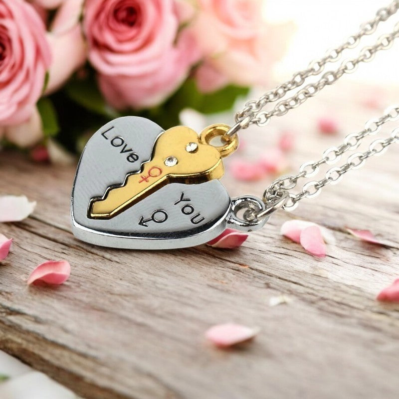A silver necklace with a key and heart pendant set on a wooden surface with pink roses in the background.