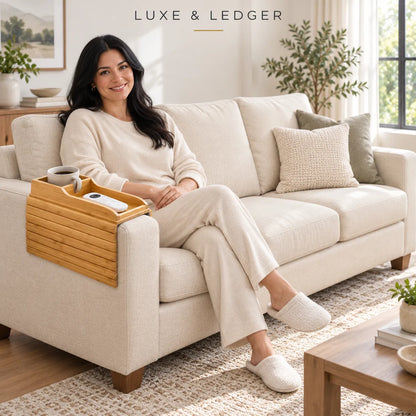 A woman in a cream lounge set sits on a light beige sofa in a bright living room, with a bamboo tray resting on the armrest. The text 'LUXE & LEDGER' appears at the top.