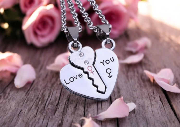 A silver necklace with a key and heart pendant set on a wooden surface with pink roses in the background.
