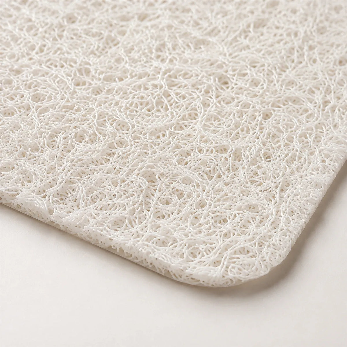 A close-up of a white textured mat with a dense, curly fibrous loop pattern, showing its corner and edge against a light neutral background.