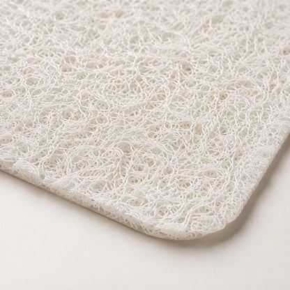 A close-up of a white textured mat with a dense, curly fibrous loop pattern, showing its corner and edge against a light neutral background.