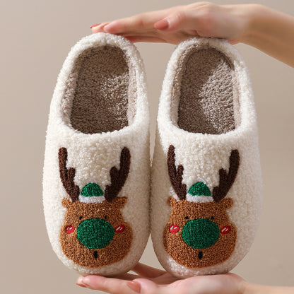 Pair of white slippers with reindeer face design held by a hand against a beige background