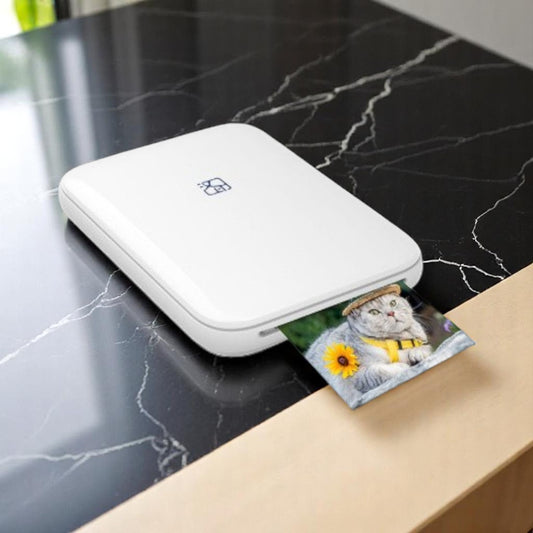 White portable photo printer on a marble surface with a printed photo of a cat and sunflower.
