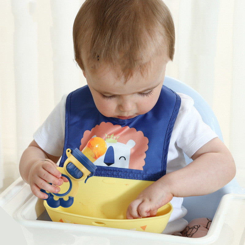 Child wearing a blue bib with a cartoon design, sitting in a high chair and holding a yellow bowl.