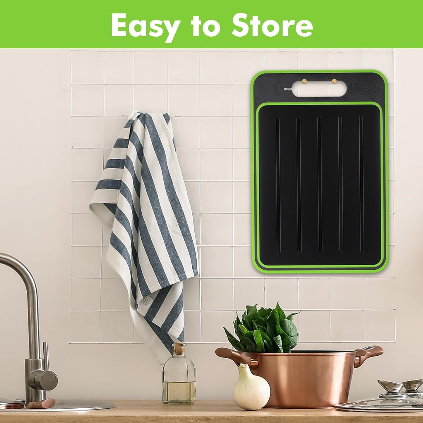 Black cutting board with green rim hanging on a kitchen wall next to a striped towel.