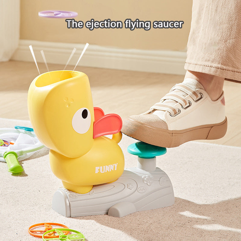 Yellow duck-shaped ejection flying saucer toy with a foot on it, on a light-colored floor.