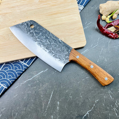 Chef's knife with wooden handle on a gray surface with a cutting board and ingredients.