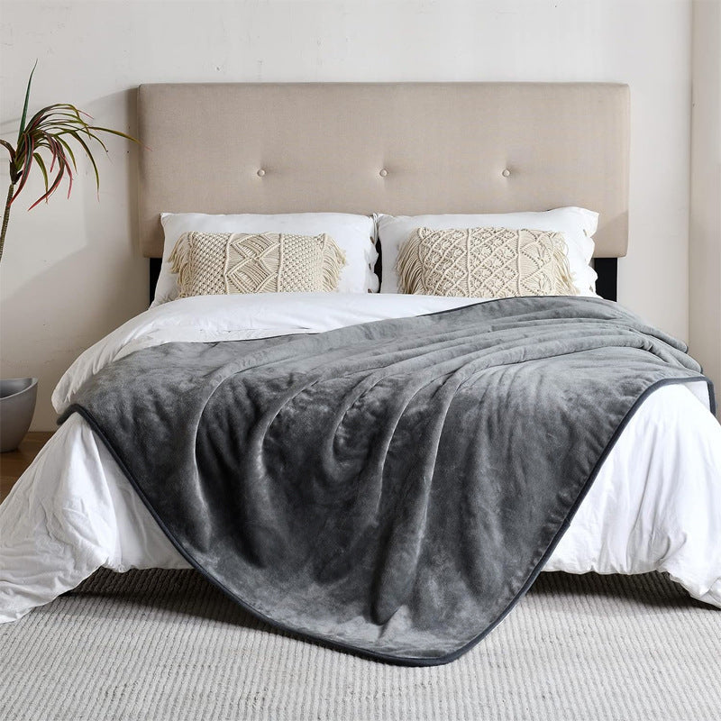 Gray blanket draped over a bed with white bedding and beige pillows in a bedroom setting.