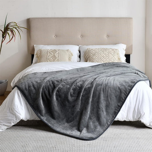 Gray blanket draped over a bed with white bedding and beige pillows in a bedroom setting.