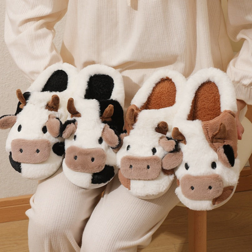 Pair of cow-themed slippers worn by a person sitting on a chair.