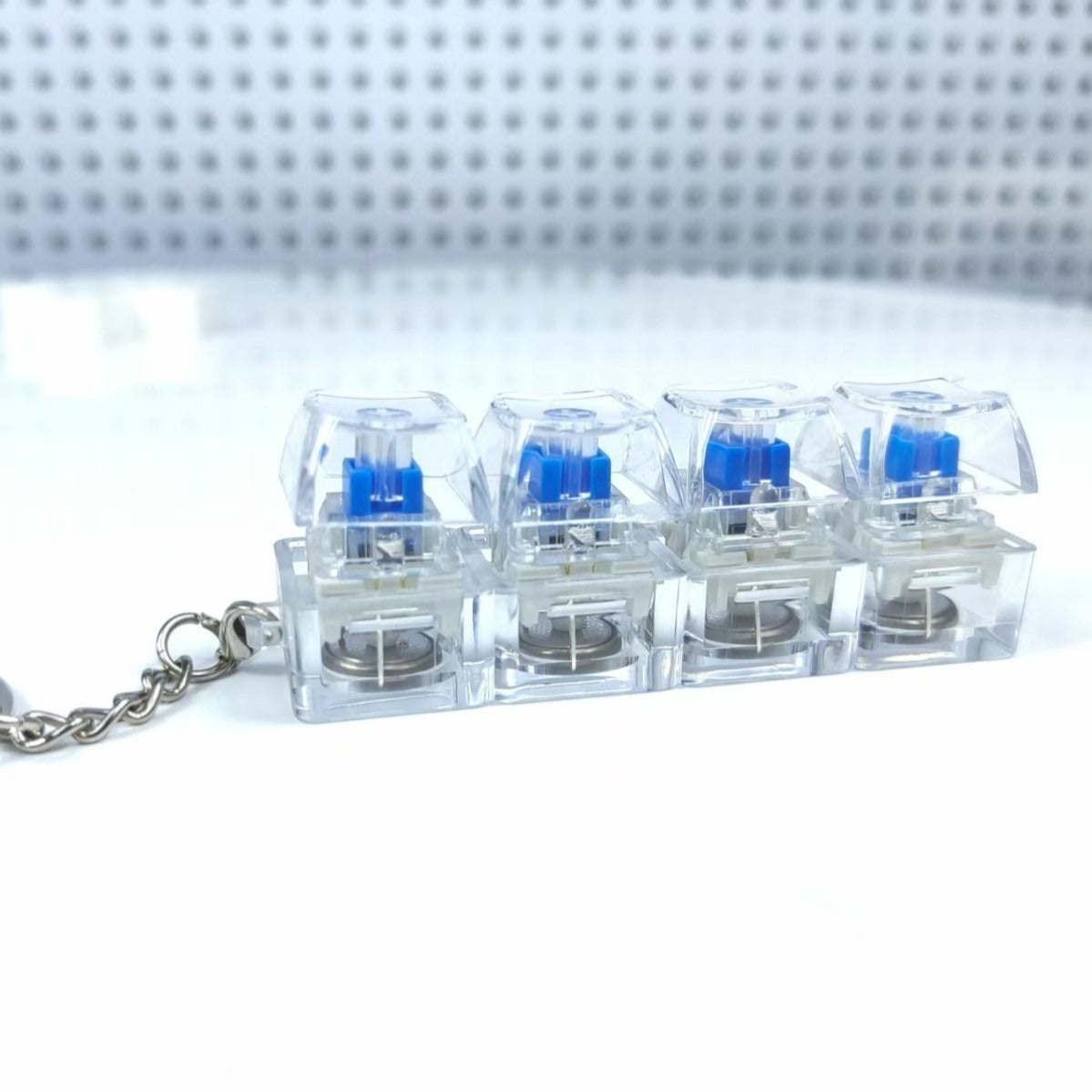 "Clear mechanical switch keychain with four blue clicky switches displayed on a white minimal backdrop