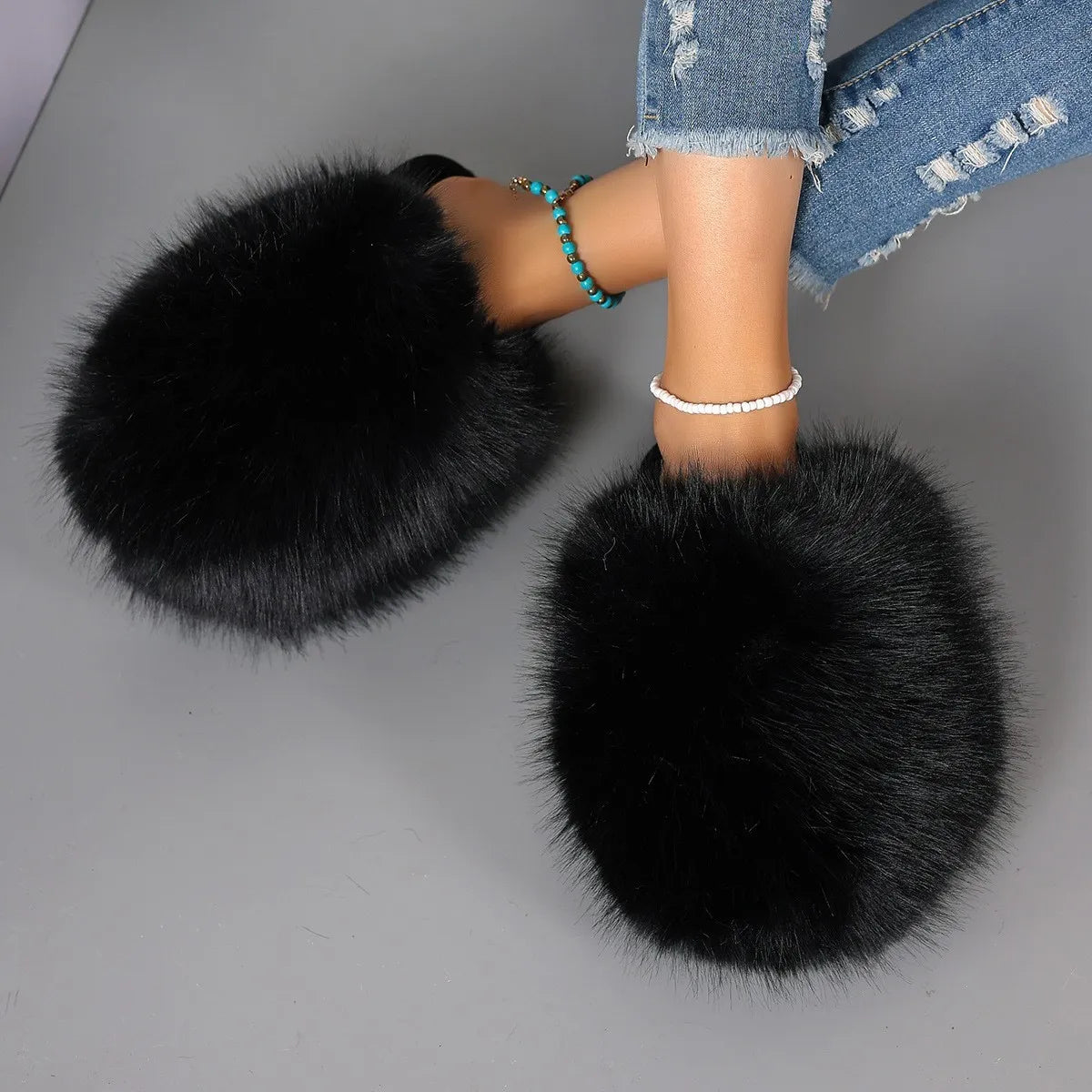 Black fluffy slippers worn with denim jeans on a gray background