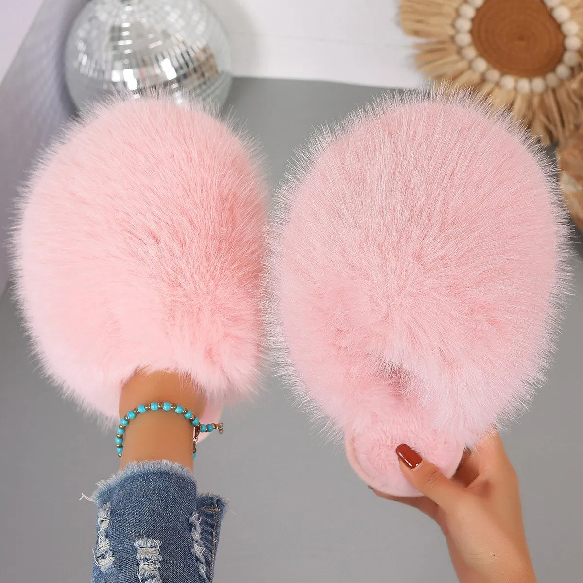 Pink fluffy slippers being held by a person with a blurred background