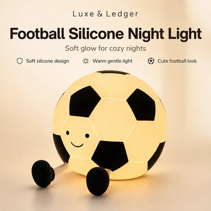 A soccer ball-shaped night light with a warm yellow glow, featuring black pentagons and hexagons, a small smiley face, and two black wheels. Text at the top reads 'Luxe & Ledger Football Silicone Night Light' with feature callouts.