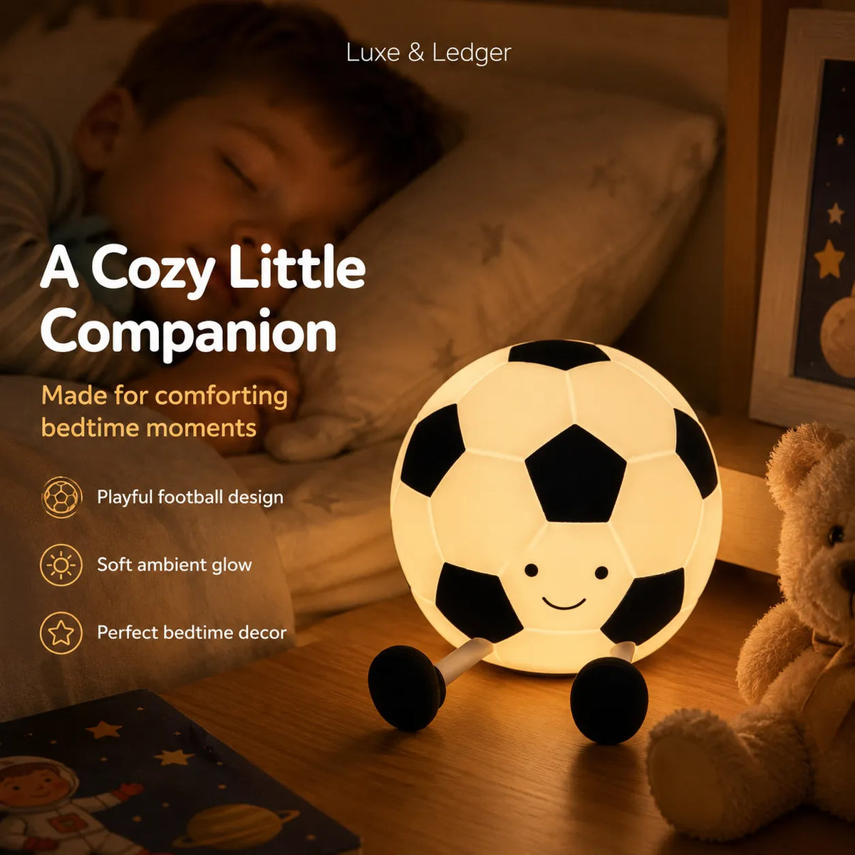 A glowing soccer ball night light with a smiling face and small wheels, placed on a wooden bedside table next to a teddy bear. A child is sleeping in the background under warm bedside lighting.