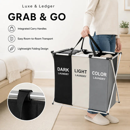 A person carries a large three-compartment laundry hamper in a bright room. The hamper has black, white, and gray fabric panels with white text reading 'DARK LAUNDRY', 'LIGHT LAUNDRY', and 'COLOR LAUNDRY'.